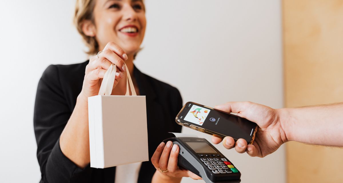 门店店员递出购物袋，顾客用手机完成支付